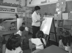 Maestra con estudiantes y rotafolios.png