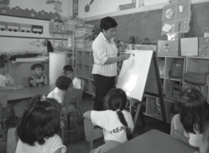 Maestra con estudiantes y rotafolios.png