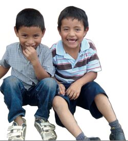 Dos niños sentados juntos, sonrientes miran a la cámara